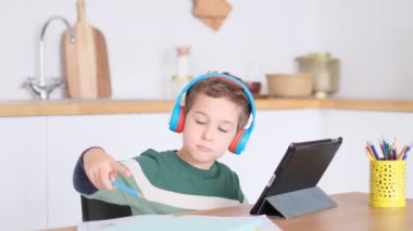 Küçük çocuk öğretmeniyle video görüşmesi yapmak için bir dizüstü bilgisayar kullanıyor. İnternette uzaktan çalışan çocuk öğretmenin defterine anlattığı dersleri yazıyor. Uzaklık eğitimi kavramı.