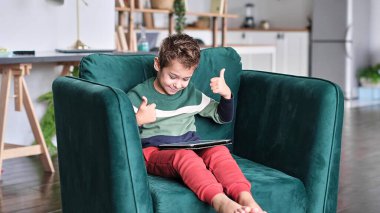 Kanepede oturup tablet kullanırken gülümseyen neşeli küçük çocuk. Modern çocuk ve eğitim teknolojisi. Küçük çocuk evdeki dokunmatik yere bakıyor..