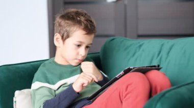 Küçük çocuk evde dijital tabletle oynarken gülümsüyor. Modern çocuk ve eğitim teknolojisi. Küçük çocuk evdeki dokunmatik yere bakıyor..