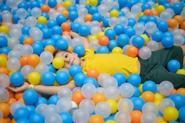 Çocuk oyun parkında renkli top havuzunda oynuyor. Parlak renklerde mutluluk.