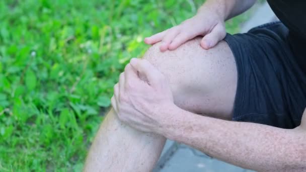 El deportista se retuerce de dolor en la pierna, se lesionó durante el entrenamiento en la calle. Él sosteniendo la rodilla mal — Vídeo de stock