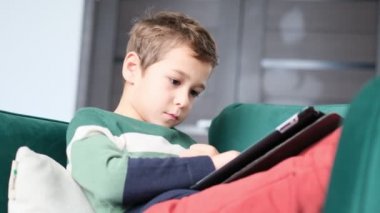 Küçük çocuk evde dijital tabletle oynarken gülümsüyor. Modern çocuk ve eğitim teknolojisi. Küçük çocuk evdeki dokunmatik yere bakıyor..