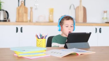 Akıllı çocuk tablet hakkında online ders dinliyor kulaklık takıyor Spbas. Evde eğitim görmüş çocuk gözetimi. Neşeli, çekici okul çocuğu.