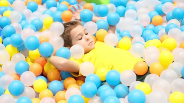 Fiú játszik játszótér színes labda medence. Boldogság élénk színekben. — Stock videók