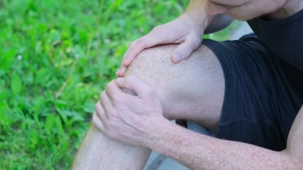Sportovec se kroutí bolestí v noze, má zranění během cvičení na ulici. Drží špatné koleno. — Stock video