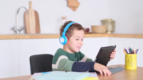 Estudante menino inteligente ouvir aula on-line sobre tablet usar fones de ouvido Spbas. Vigia de crianças em casa. alegre, encantador estudante — Vídeo de Stock