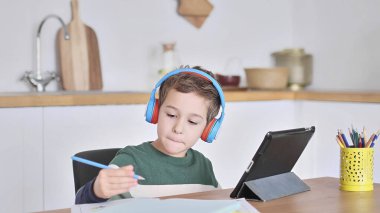 Akıllı çocuk tablet hakkında online ders dinliyor kulaklık takıyor Spbas. Evde eğitim görmüş çocuk gözetimi.