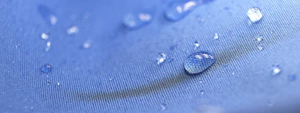 Σταγόνες νερού στο ύφασμα. Σταγονίδια νερού βροχής σε αδιάβροχο ύφασμα μπλε ίνας. Νερό σταγόνες μοτίβο πάνω από ένα αδιάβροχο πανί. Μπλε φόντο. — Φωτογραφία Αρχείου