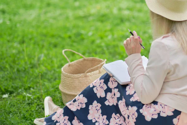 Mulher com caneta escrita no notebook na grama fora. — Fotografia de Stock