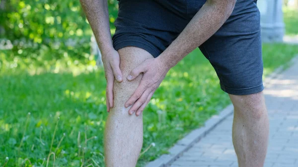 Hombre atleta corredor tocando el pie en el dolor debido a un esguince de tobillo. atleta irreconocible se sienta en el suelo y sufre de dolor de rodilla — Foto de Stock
