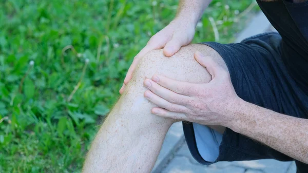 Hombre atleta corredor tocando el pie en el dolor debido a un esguince de tobillo. atleta irreconocible se sienta en el suelo y sufre de dolor de rodilla — Foto de Stock