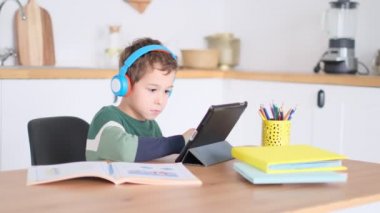 Akıllı çocuk tablet hakkında online ders dinliyor kulaklık takıyor Spbas. Evde eğitim görmüş çocuk gözetimi. Neşeli, çekici okul çocuğu.