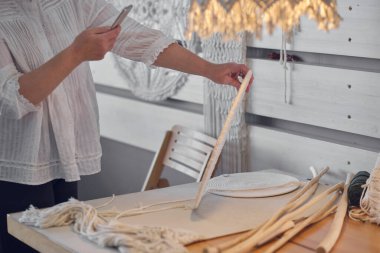 Sanatçı kadın internette satılık ürünlerini fotoğraflıyor. Gelir kaynağı olarak hobi. Yaşlı kadın telefonda nakışlarını çıkarıp sosyal ağlara yüklüyor.