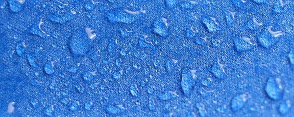 Wasser tropft auf den Stoff. Regenwassertropfen auf blauem, faserdichtem Gewebe. Wassertropfen ziehen sich über ein wasserdichtes Tuch. Blauer Hintergrund. — Stockfoto