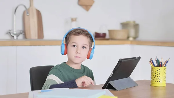 Étudiant garçon intelligent écouter des leçons en ligne sur tablette porter casque Spbas. Montre enfant à domicile. — Photo