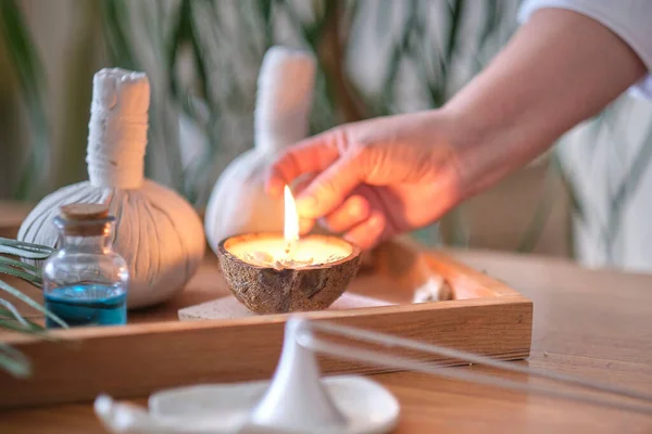 Bougie au parfum de noix de coco sur une table en bois. Beau concept de spa tropical. Pochettes en coton avec des herbes pour massage sur fond de bois avec des feuilles vertes. Boules de compression à base de plantes — Photo