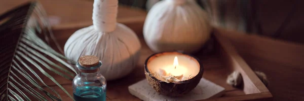 Vela con el aroma de coco en una mesa de madera. Hermoso concepto de spa tropical. Bolsas de algodón con hierbas para masaje sobre fondo de madera con hojas verdes. Bolas de compresa de hierbas — Foto de Stock