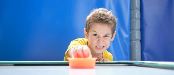 Ragazzo intensamente e con entusiasmo giocare a hockey da tavolo.. Un bambino che ha vinto la sua partita di hockey aria, con un martello rosso in mano. — Foto Stock