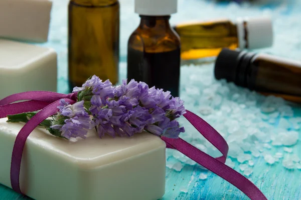 Natuurlijke biologische zeep flessen etherische olie en zeezout op een blauwe houten tafel, met bloemen — Stockfoto