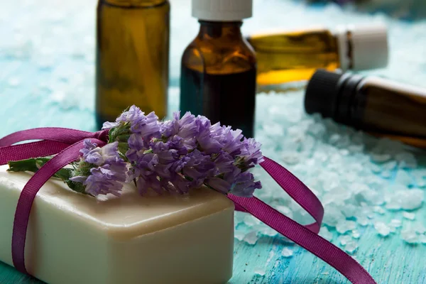Természetes szerves szappan palackok illóolaj és a tengeri só a kék fából készült asztal, virágok — Stock Fotó