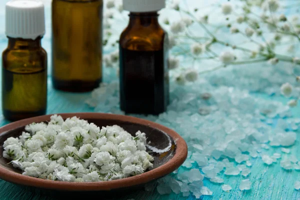 Bouteilles huile essentielle et sel de mer sur une table en bois bleu, avec des fleurs — Photo