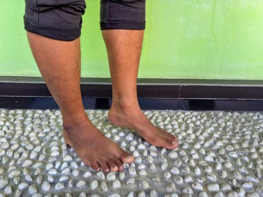 Evdeki refleksoloji tedavisi için Endonezyalı erkek ayağının beton zemine yakın çekimi, sinirleri canlandırmak ve doğal olarak sağlık ve rahatlamayı teşvik etmek.
