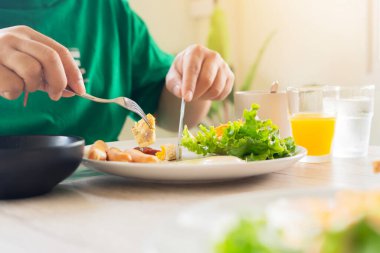 Evde sağlıklı bir kahvaltı yapan, taze sebze, sosis yiyen, kahve içen, mutfak masasında oturan bir adam.