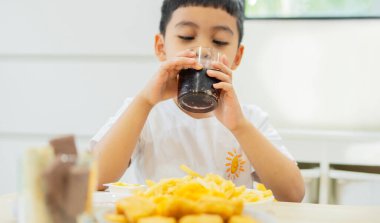 Asyalı elinde zararlı içecekler tutuyor ve evde atıştırmalık yiyor. Fast food konsepti. Mide iltihabının nedeni olarak sağlıksız beslenme.
