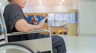 Hastanedeki tekerlekli sandalyede oturup fotokopi çekerken cep telefonu kullanan Asyalı yaşlı bir kadının yan görüntüsü. Seçici odak.