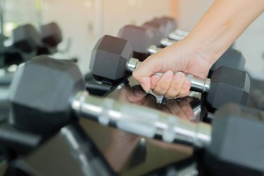 Spor salonundaki raftan bir kadın elinin dambılına uzanırken yakın plan çekimleri.