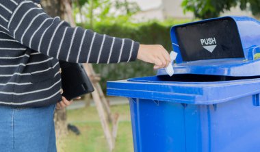 Parktaki geri dönüşüm kutusuna kağıt atan bir kadının yan görüntüsü. Çevre koruma ve geri dönüşüm kavramı.