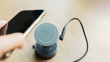 El, cep telefonunu kablosuz şarj cihazına, tahta masada fotokopi alanı olan bir yere koyar. Kablosuz şarj cihazının yanındaki cep telefonu Modern yaşam tarzı teknoloji kavramı.