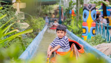 Mutlu gülümseyen Asyalı çocuk kameraya bakıyor ve lunaparkta su üstünde kürek çekiyor. Çocuklar konsept oynar.