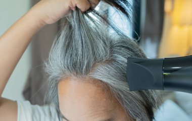 Olgun bir Asyalı kadın kısa gri saçlarını evde saç kurutma makinesiyle kurutuyor. Fırça ve kurutma makinesiyle saç rutini. Saç kurutma makinesi. Saç bakım konsepti. Saç stili ve saç kurutma makinesi. Rutin.