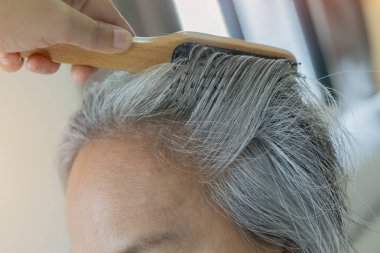 Beyaz saçlı ve saçını evde tarayan Asyalı olgun bir kadın. Saç ve yaşın doğal grileşmesi. Seçici odak.