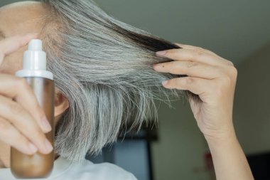 Saçları ağarmış ve saç serumu kullanan olgun bir kadın. Seçici odaklanma, olgun güzellik ve kendine bakım rutin konsepti