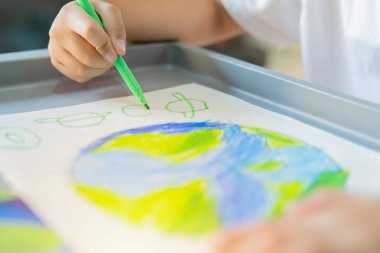 Çocuklar dünyanın resimlerini çiziyor, çocuk eli renkli kalem şeklinde çiziliyor yaratıcılığı ve sürdürülebilirliği öğrenme gününü temsil ediyor. Seçici odak.