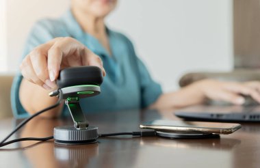 Kulaklık takan bir kadın cep telefonunun yanında kablosuz şarjla şarj oluyor. Seçici odaklanma. Modern işyeri aygıtı kavramı.