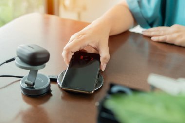 Kadın, iş yerindeki kablosuz bir şarj cihazının yanına bir kulaklığı kablosuz ped ile şarj etmiş. Teknoloji, çoklu paylaşım ve yaşam tarzı kavramları