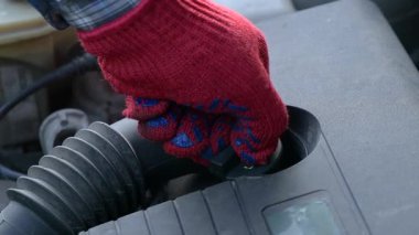 Adam garajda rutin bakım için araba motoruna yağ ekliyor. Adam yağ kepini çıkarıyor ve düzgün çalışması ve hasarı önlemek için motoru yağ ile dolduruyor.