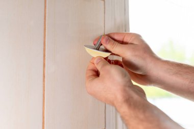 Erkek eller kancayı yapıştırmaya hazırlanıyor. Yapıştırıcı tabanından koruyucu bandı kaldıran ellerin yakın çekimi, kurulum için hazırlık sürecini gösterir ve ev alanını geliştirir.