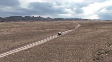 Arka planda dağlarla bozkırda giden araba.