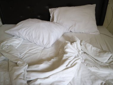 Yatak odasında kabarık yastıklar ve buruşuk çarşaflar olan bembeyaz yatak, ev dekorasyonu ve yaşam tarzı içeriği için ideal rahat ve rahat bir atmosfer yaratır..