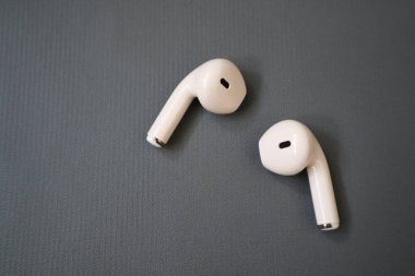 Kablosuz beyaz kulaklıklar gri desenli bir yüzeye yerleştirilir. Yumuşak ışıklandırma, teknoloji ve ses ürünleri pazarlaması için uygun temiz ve modern bir görünüm yaratır..