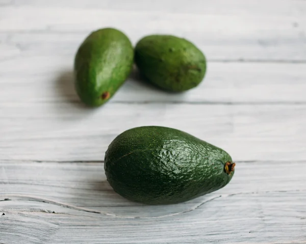 Beyaz eski ahşap bir masa üzerinde üç avokado — Stok fotoğraf