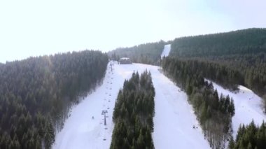 Karlı dağ yamaçları ve kış ağaçları olan kayak merkezinin hava manzarası. Stok görüntüleri. Kablo istasyonunun üst katında ve bir grup insan kayak yapmaya ve tepeden aşağıya kayak yapmaya gidiyor.