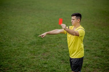 Angry football referee showing a red card and pointing with his hand on penalty. clipart