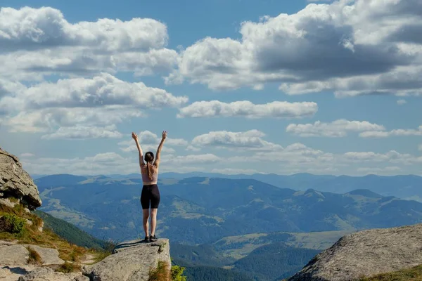 The young Woman at the top of the mountain raised her hands up on blue sky background. The woman climbed to the top and enjoyed her success. Back view.