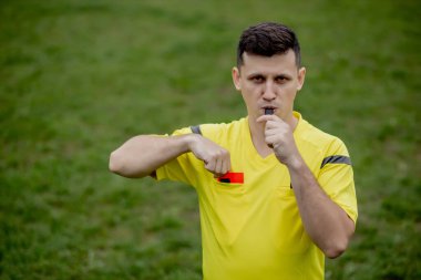 Hakem, hoşnutsuz bir futbol oyuncusu ya da futbolcuya kırmızı kart gösteriyor. Spor anlayışı, kural ihlali, tartışmalı konular, engellerin aşılması