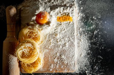 Taze pişmiş makarna, un tozuyla kaplanmış karanlık bir yüzeyde yatıyor. İtalyan makarnası. Tagliatelle. Çiğ makarna. İtalyan makarna tarifi. Üst görünüm, alanı kopyala.